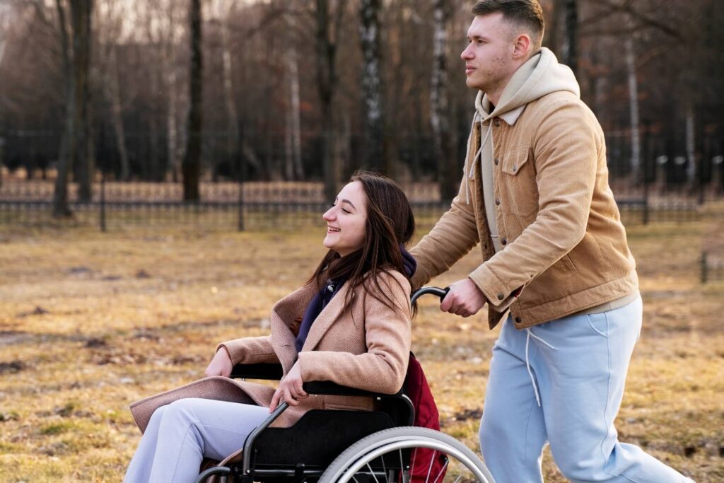 na zdjęciu osoba na wózku inwalidzkim pchana przez asystenta